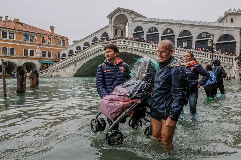 سياح يحملون عربة أطفال عبر مياه الفيضان بالقرب من جسر ريالتو في البندقية