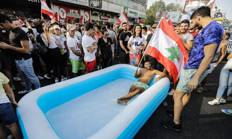 متظاهر لبناني يحمل العلم ويجلس في بركة على طريق سريع يربط بيروت بشمال لبنان